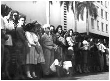 En las aceras, la multitud se agolpa. Las mujeres codo a codo con los hombres; los negros con los blancos, los jóvenes con los viejos. Y los niños se sientan en el piso para soportar la espera. En todo hay orden; pese a la enorme multitud no fue necesario un cordón, ni un soldado